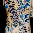 Japanese back piece tattoo by Alex Binnie of golden tiger with blue water background and cherry blossom leaves