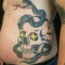 large skull and snake tattoo on mans side with yellow diamond eyes on skull