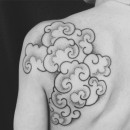 hand poke tattoo on mans shoulder of black and grey asian style clouds