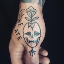 hand tattoo of simple skull with flower growing out of it and writing saying I’ll be late